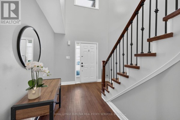 Foyer with a console table, round mirror, white door, and wooden staircase. - 89 - 4055 Forest Run Avenue, Burlington