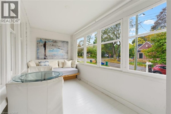 Interior sunroom with white walls and floors, a daybed, glass-topped table, and a street view through large windows. - 89 Allen Street W, Waterloo