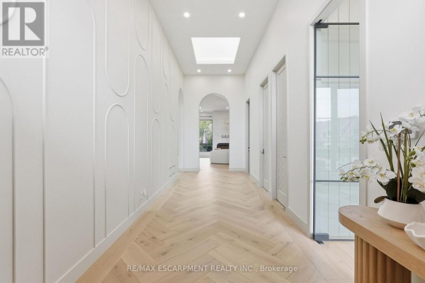 Bright white hallway with a skylight, herringbone wood floors, and arched wall details. - 89 Cumberland Drive, Mississauga