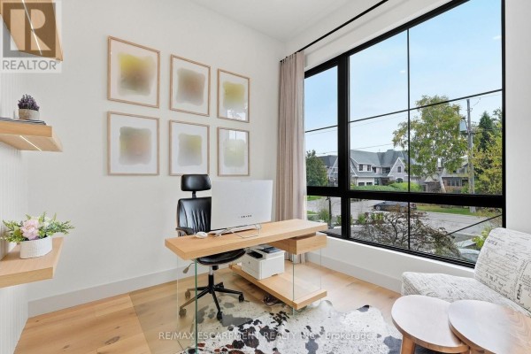 Home office with a large window overlooking the street, a wooden desk, and framed artwork. - 89 Cumberland Drive, Mississauga