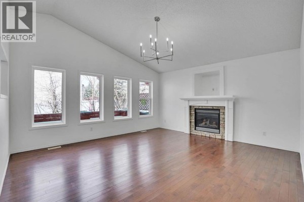 Empty living room with vaulted ceiling, gas fireplace with stone surround, and dark wood floors. - 89 Everoak Drive Sw, Calgary