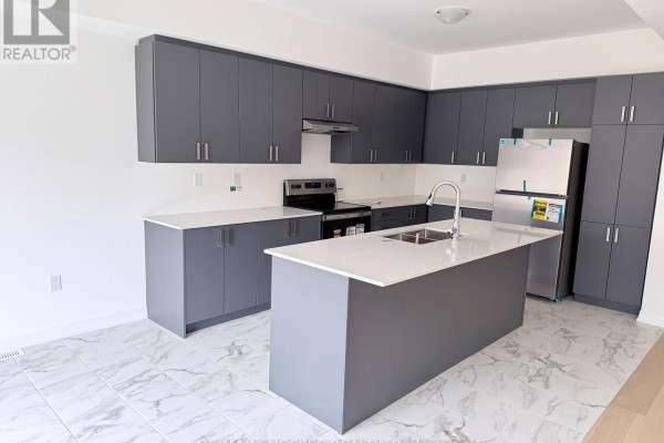 Modern kitchen with grey cabinets, stainless steel appliances, quartz countertops, and a large island. - 89 Flan Boulevard, Barrie