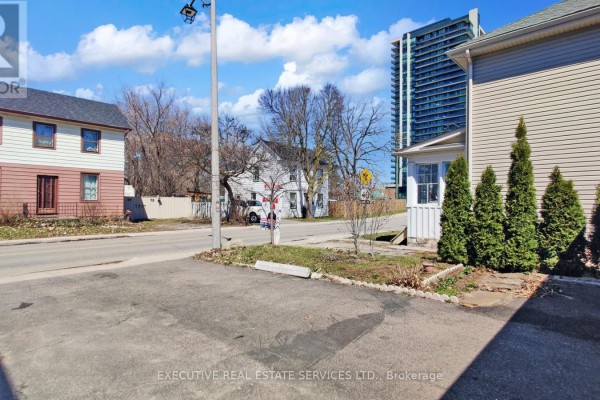 Two-story house with driveway and trees, next to a modern high-rise - 89 John Street Brampton