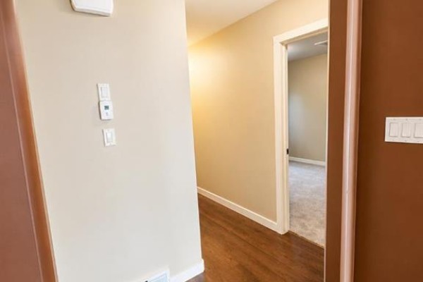 Hallway with light beige walls and a view into a carpeted room. - 89 Lynx Road N, Lethbridge