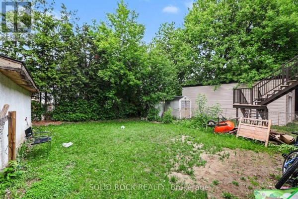 Backyard with a green lawn, mature trees, and a small shed. - 89 Marier Avenue, Ottawa