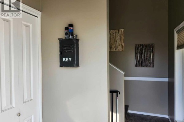 Interior hallway with beige walls, a black key holder, and artwork on the walls. - 89 Poplar Street, Drumheller