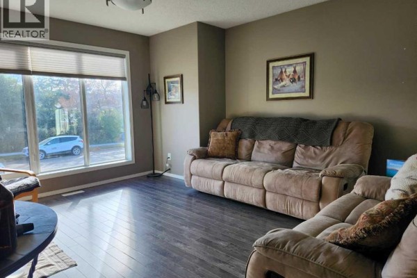 Living room with a large window overlooking the street, beige recliner sofas, and dark hardwood floors. - 89 Poplar Street, Drumheller