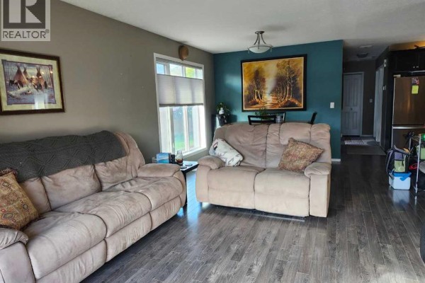 Living room with beige sofas, dark hardwood floors, and a blue accent wall with artwork. - 89 Poplar Street, Drumheller