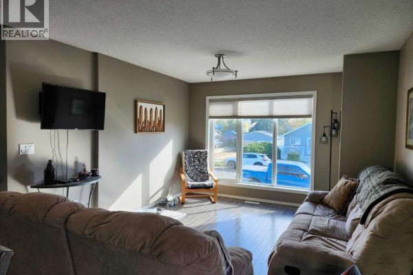 Living room with a television mounted on the wall, sofas, and a large window with street view. - 89 Poplar Street, Drumheller