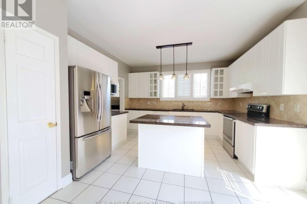 A modern white kitchen with stainless steel appliances, a granite island, and tiled flooring. - 89 Skywood Drive, Richmond Hill