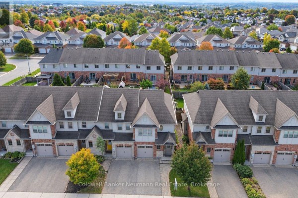 Aerial view of a row of townhouses with manicured lawns and mature trees. - 89 Washburn Drive, Guelph