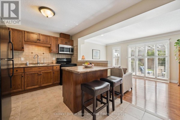 Open concept kitchen and living area with dark wood cabinets, island with stools, and patio doors. - 89 Washburn Drive, Guelph