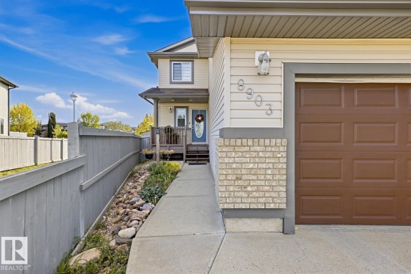 Close-up view of the entrance to a beige house with a brown garage door and a paved walkway. - 8903 176 Av Nw, Edmonton