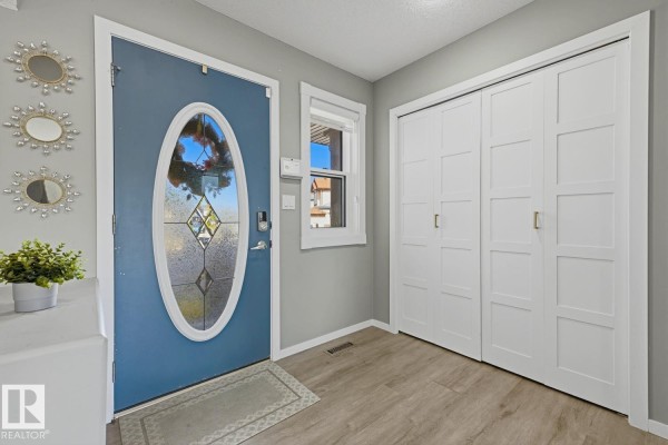 Interior view of a foyer with a blue front door, closet doors, and light grey walls. - 8903 176 Av Nw, Edmonton