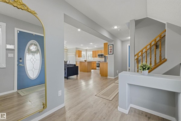 View from the foyer into the living area, kitchen, and staircase of a house with light grey walls. - 8903 176 Av Nw, Edmonton