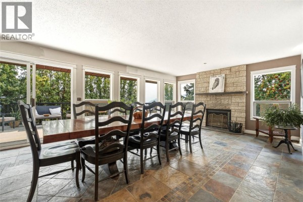 Spacious dining room with a long wooden table, chairs, stone fireplace, and large windows. - 8905 Russet Drive, Vernon