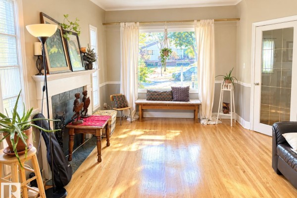 Living room with a fireplace, large window, and hardwood floors. - 8907 83 Av Nw, Edmonton
