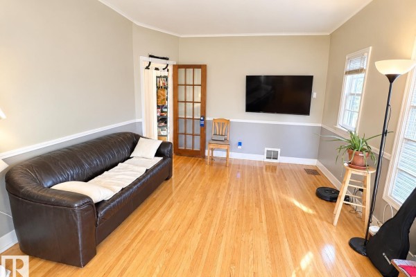 Living room with dark leather sofa, hardwood floors, and television. - 8907 83 Av Nw, Edmonton