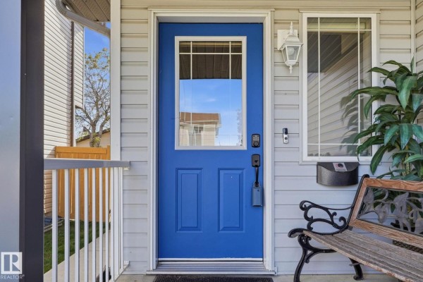 Close-up of a bright blue front door with a glass pane, flanked by windows and a metal bench. - 8911 173 Av Nw, Edmonton