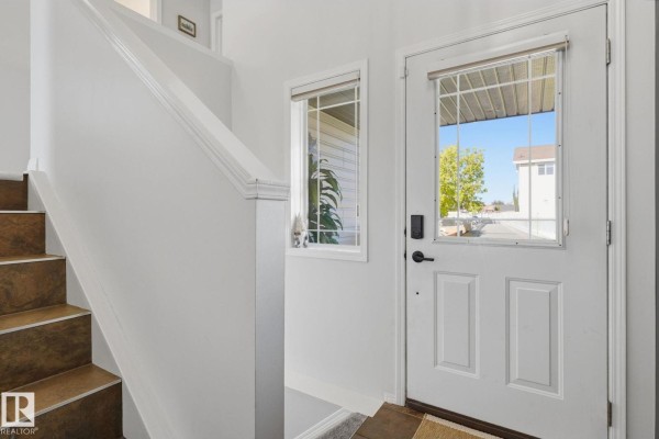 Interior view of a white entryway with a staircase to the left and a white door with a glass pane to the right. - 8911 173 Av Nw, Edmonton