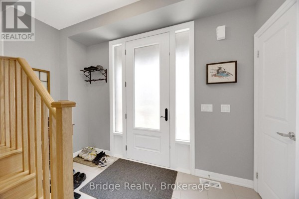 Interior foyer with a light grey wall, white door, wooden staircase, and frosted glass front door. - 892 Sobeski Avenue, Woodstock