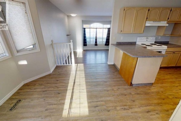 Kitchen island and cabinetry with light wood doors and a white stovetop. View of living area. - 8929 108 Avenue, Grande Prairie