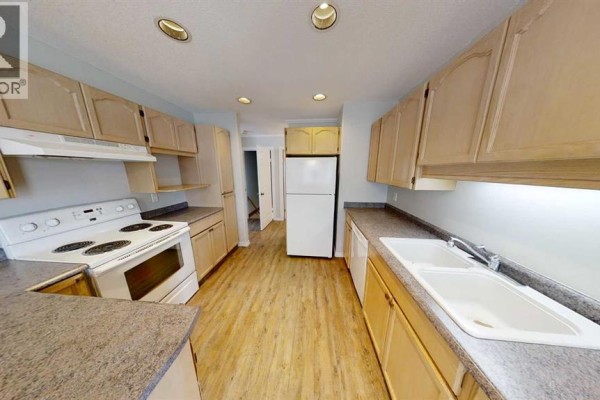Long kitchen with light wood cabinets, white countertops, a double sink, and white appliances. - 8929 108 Avenue, Grande Prairie