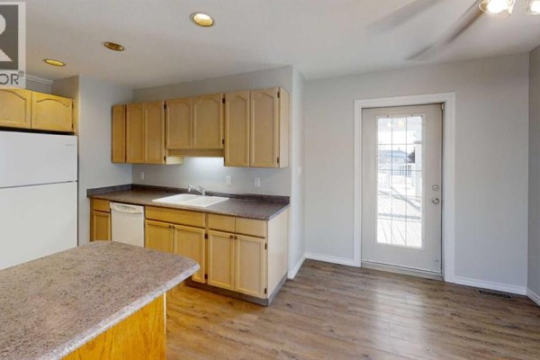 Kitchen island, light wood cabinets, white sink, white dishwasher, and a glass door to the outside. - 8929 108 Avenue, Grande Prairie