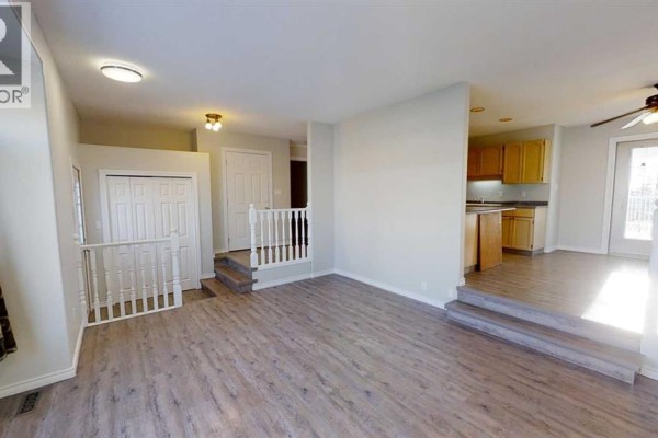 Living room with light grey walls, wood laminate flooring, and stairs leading to the kitchen area. - 8929 108 Avenue, Grande Prairie