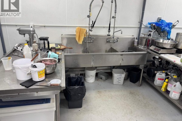 Commercial kitchen area with a large stainless steel double sink, commercial mixer, buckets, and food processing equipment. - 8940 Douglas Street, Richmond