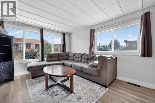 Living room with a sectional sofa, coffee table, large windows, and a rug. - 8945 Hwy 97n Highway Unit# 34, Kelowna