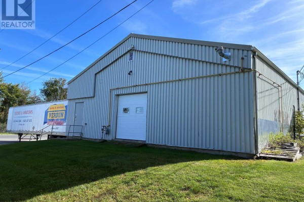 Side exterior of a commercial building with corrugated metal siding and a white overhead garage door. - 896 Cecile Boulevard, Hawkesbury