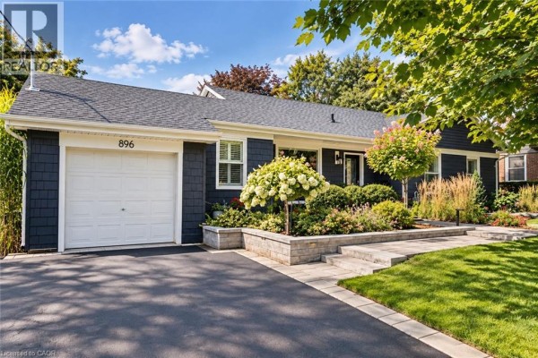 Close-up exterior of a dark grey bungalow with a white garage door, stone walkway, and landscaping. - 896 Eagle Drive, Burlington