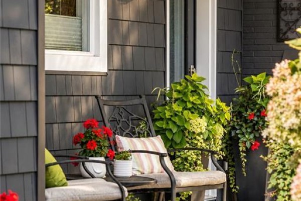 Two outdoor chairs with cushions and plants on a small porch with dark grey siding. - 896 Eagle Drive, Burlington