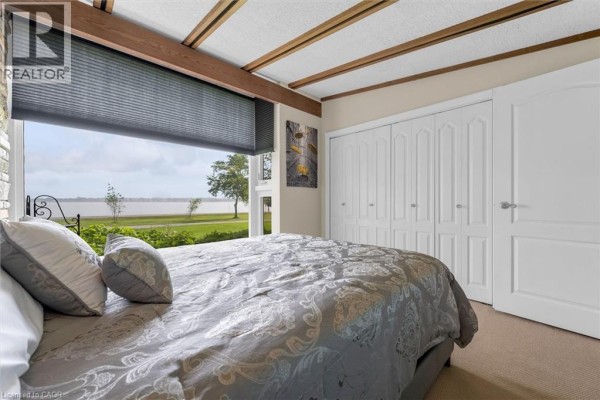 Bedroom with a large bed, white closet doors, and a panoramic window view of water and trees. - 899 Niagara Parkway, Fort Erie