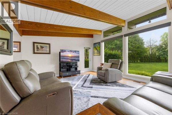 Living room with leather recliners, a television, and large windows overlooking a grassy backyard. - 899 Niagara Parkway, Fort Erie