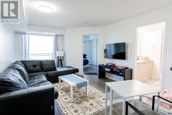 Living room with a black sectional sofa, coffee table, rug, dining table, and television. - 8a - 310 Central Park Drive, Ottawa