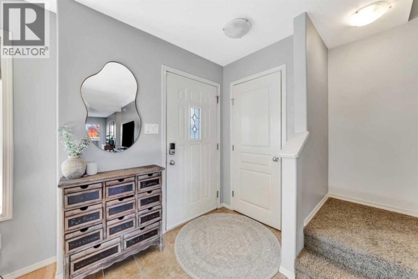 Entranceway with beige tiled floor, white doors, mirrored cabinet, and carpeted stairs. - 9, 4738 13 Street, Lloydminster