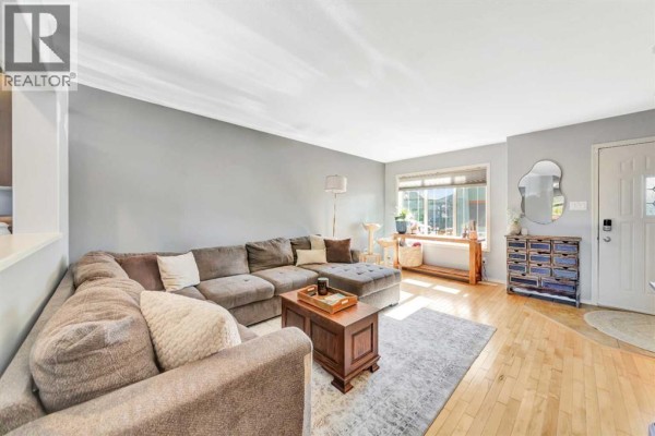 Living room with grey walls, sectional sofa, wood floor, large window, and coffee table. - 9, 4738 13 Street, Lloydminster