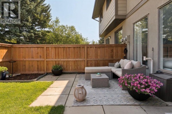 Patio view with sectional couch, rug, planter, and wooden fence background. - 9, 5019 46 Avenue Sw, Calgary
