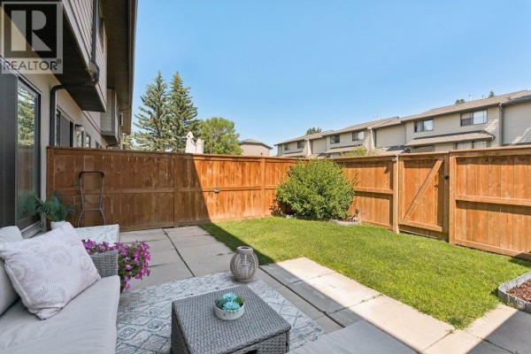 Fenced backyard with patio, grass, and a shed on the right. - 9, 5019 46 Avenue Sw, Calgary