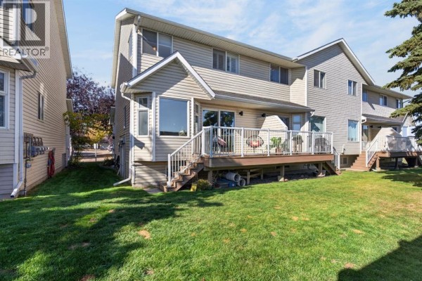 Backyard view of townhouse with a wooden deck and grass lawn. - 9, 567 Edmonton Trail Ne, Airdrie