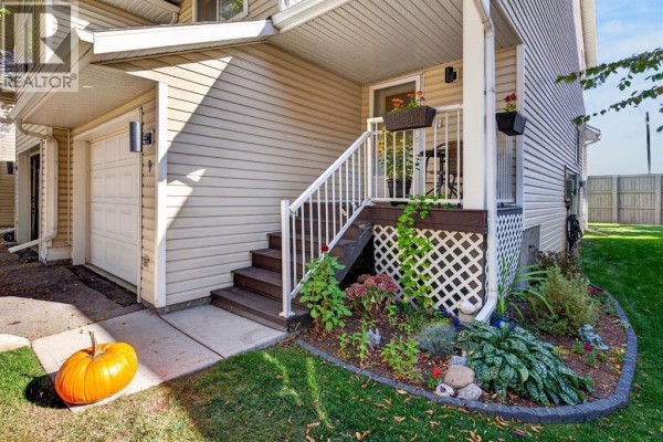 Close-up of townhouse front entrance with stairs, flower beds, and pumpkin decoration. - 9, 567 Edmonton Trail Ne, Airdrie