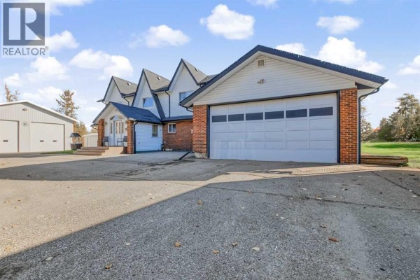 Side view of a house with a white siding and brick exterior, featuring a double garage door. - 9, 710072 40 Highway, Rural Grande Prairie No  1, County Of