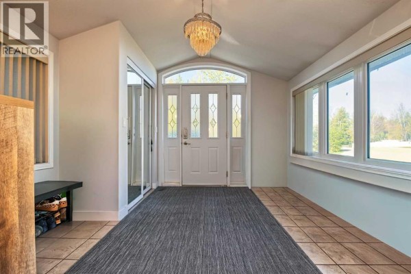 Interior view of a bright sunroom with large windows, a gray rug, and a chandelier above the front door. - 9, 710072 40 Highway, Rural Grande Prairie No  1, County Of