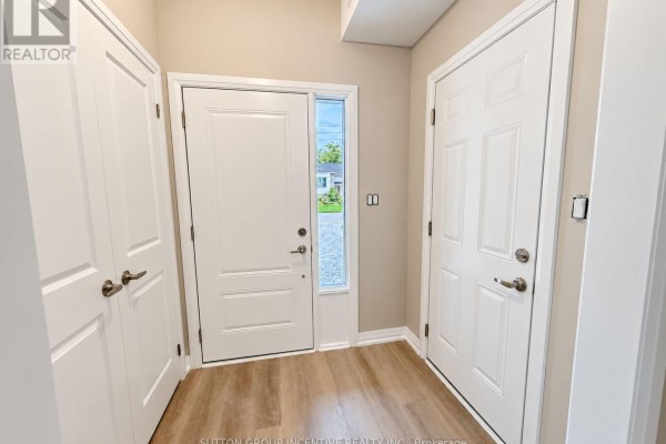 Interior foyer with beige walls, two white doors, a front door with a window, and light wood flooring. - 9 - 1 Riverdale Drive, Wasaga Beach