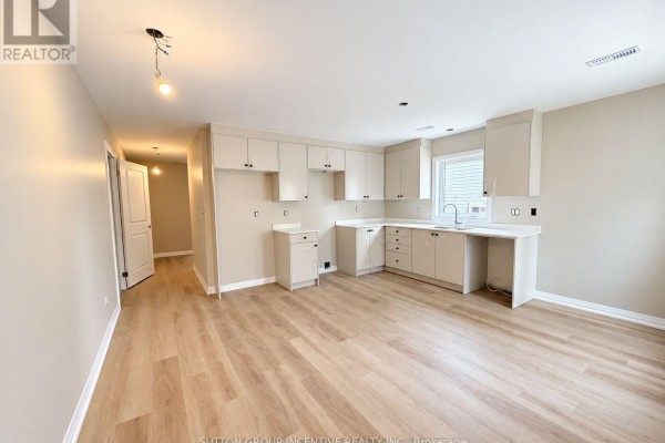 Unfinished open-concept kitchen and living area with light wood floors, beige walls, and white cabinets. - 9 - 1 Riverdale Drive, Wasaga Beach