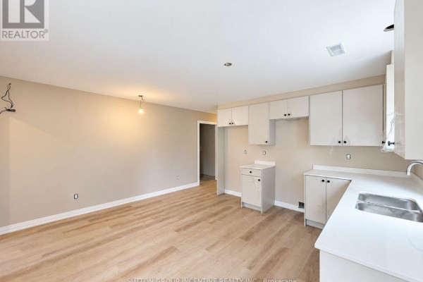 Kitchen area with white cabinets, light wood floors, and beige walls, leading to a hallway. - 9 - 1 Riverdale Drive, Wasaga Beach