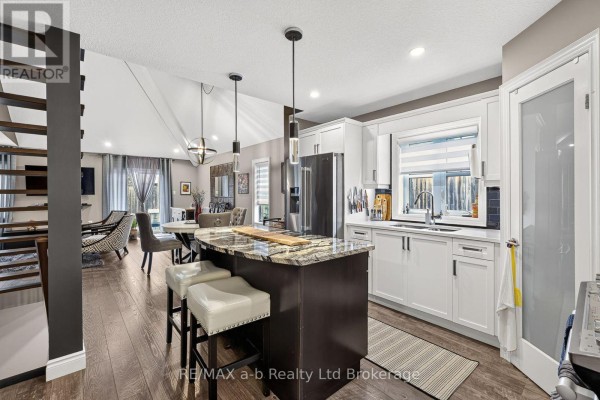 Open concept kitchen with white cabinets, granite island, and pendant lights. - 9 - 175 Ingersoll Street N, Ingersoll