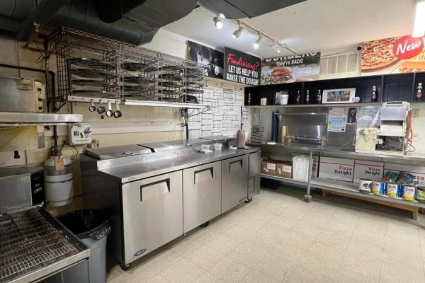 Commercial kitchen with stainless steel prep tables, pizza racks, ovens, and shelves of supplies. - 9 - 181 St Andrew Street E, Centre Wellington